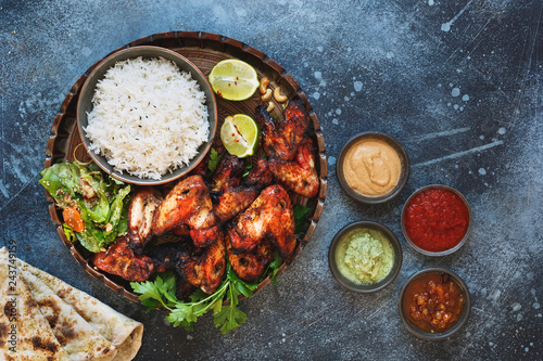 Tandoori chicken wings served with pilau rice, soft garlic cheese naan with different chutney dipping sauces. Top view, blank space, rustic background