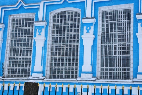 three large old windows with iron bars on the blue white wall of the building behind the black fence