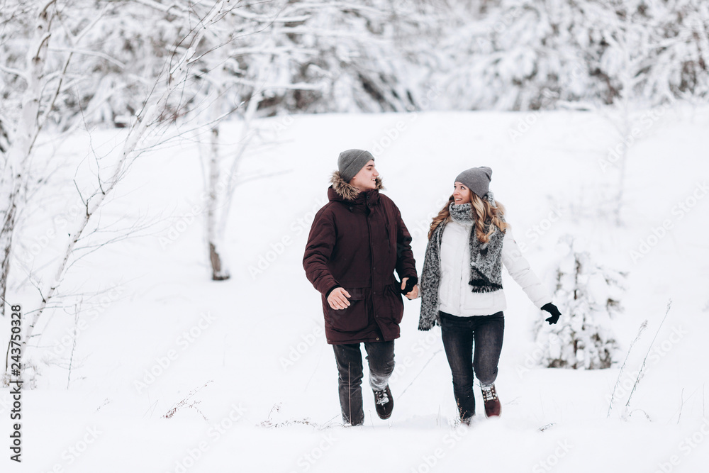 Young couple running on a snowy winter field near pine