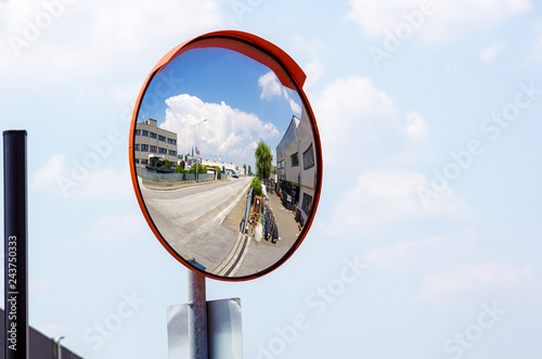 Outdoor convex safety mirror hanging on wall with reflection of an urban roadside view of cars parked along the street by residential apartment buildings. photo
