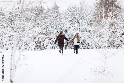 Young couple running on a snowy winter field near pine