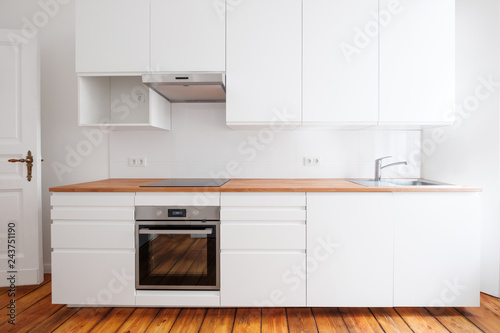 white kitchenette , newly built-in kitchen furniture frontal view with wooden worktop and board floor photo