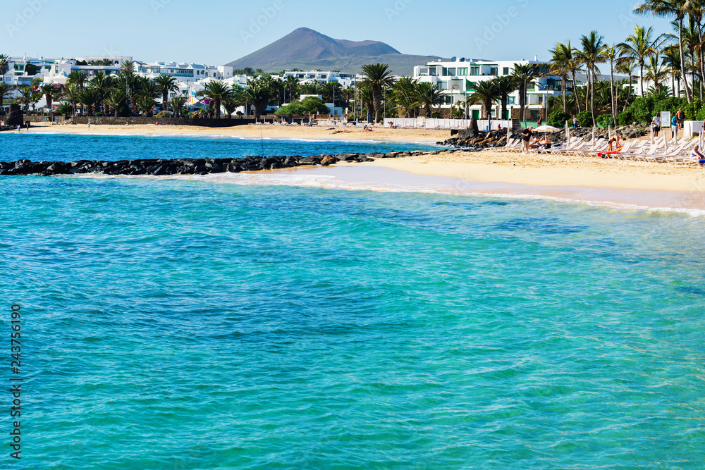 Turquoise waters in Las Cucharas beach, Lanzarote, Canary islands. VIew of the sea, sandy beach and mountains, selective focus