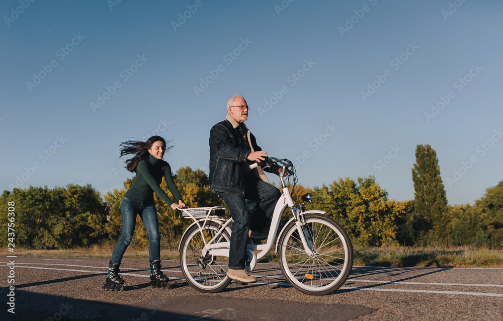 Girl on roller skates and a man on a bike fun ride together. Active leisure and hobbies. Father and daughter.