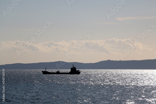 Silhouette of an industrial ship on a sunny day. Sunlight reflects on he sea.