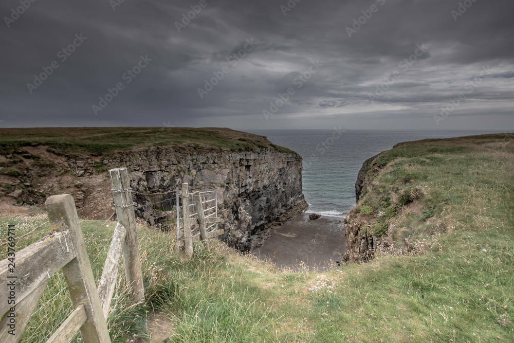 Fototapeta premium Limestone quarry on Pembrokeshire coast, Uk.Cliff top with fence and moody sky above sea.Landscape scene with copy space.