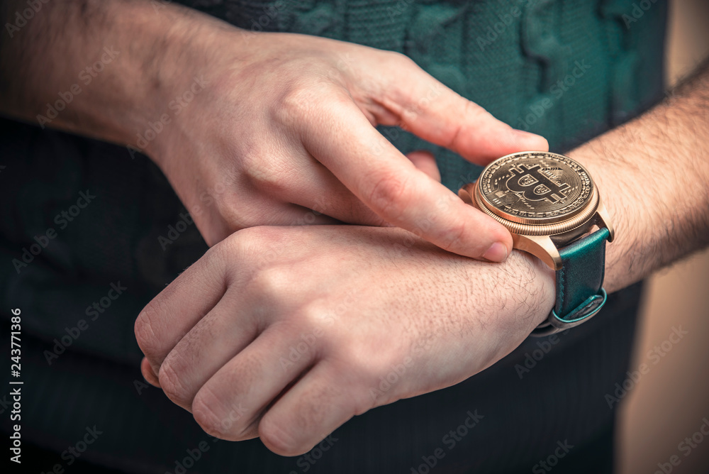 Young man's hands setting watch with a bitcoin golden penny, time to act concept Young man's hands setting watch with a bitcoin golden penny, time to act concept
