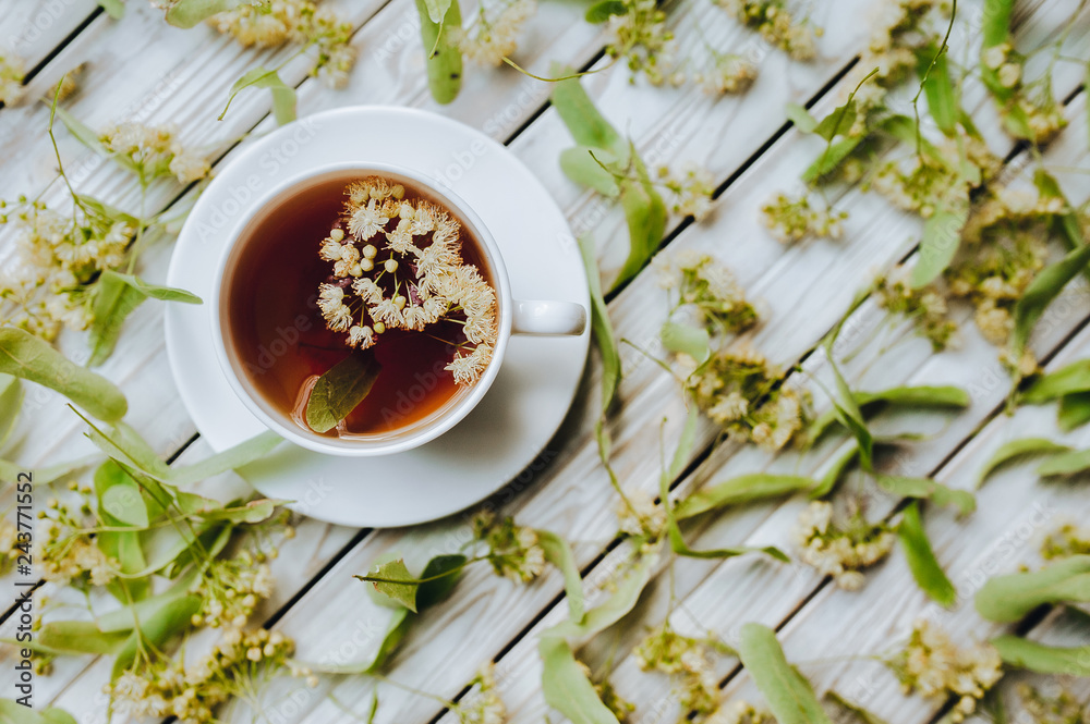 White cup of linden tea on linden blossom background. Herbal medicine. Top view. Treatment of cold and flu concept.