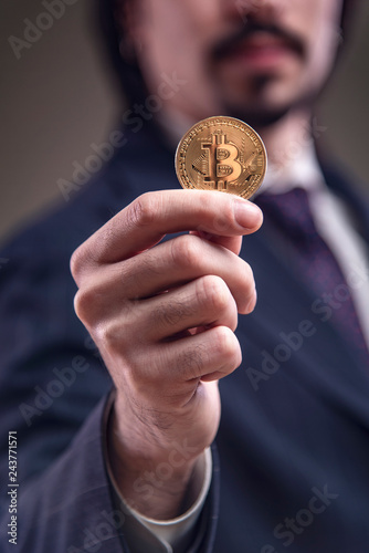 Confident business man holding a golden bitcoin in his hand, showing its value