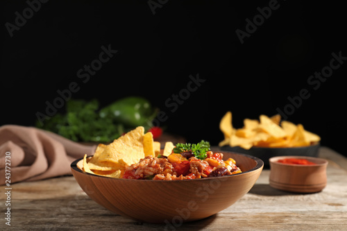 Tasty chili con carne served with tortilla chips in bowl on table
