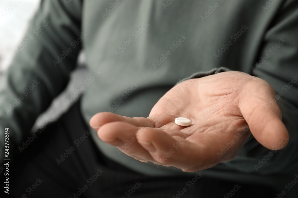 Fototapeta premium Senior man holding pill in his hand, closeup