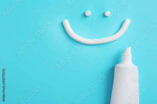 Smiling face made of toothpaste, tube and space for text on color background, top view