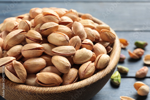 Organic pistachio nuts in bowl on wooden table, closeup