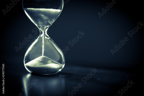 Hourglass as time passing concept for business deadline, urgency and running out of time. Sandglass, egg timer on dark background showing the last second or last minute or time out.  With copy space.