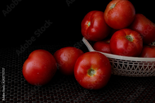 Fresh tomatoes on a plate on a dark background. a basket full of tomatoes. - Image