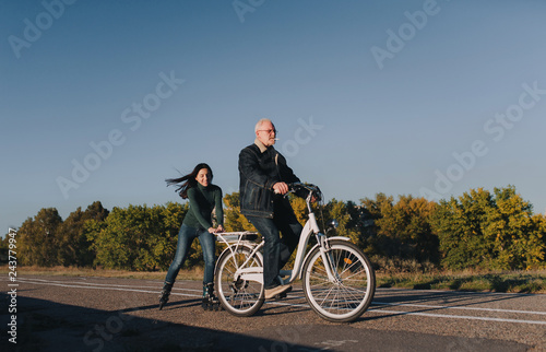 Girl on roller skates and a man on a bike fun ride together. Active leisure and hobbies. Father and daughter.