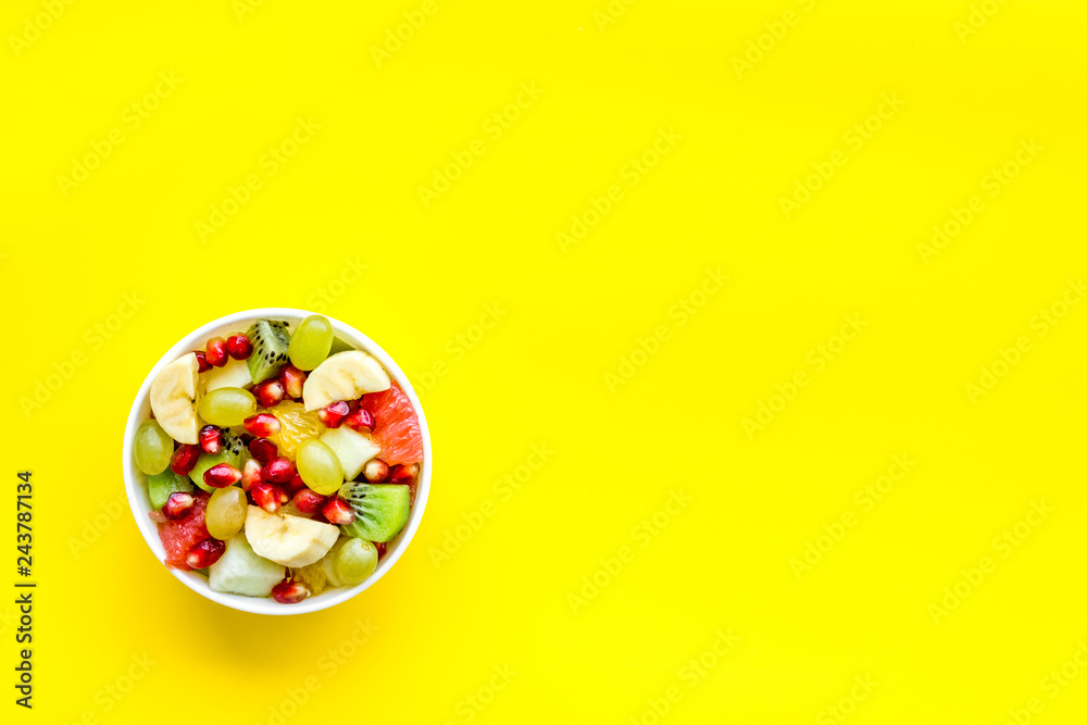 Light healthy breakfast or appetizer. Fruit salad with apple, kiwi and pomegranate in bowl on yellow background top view copy space Light healthy breakfast or appetizer. Fruit salad with apple, kiwi and pomegranate in bowl on yellow background top view copy space