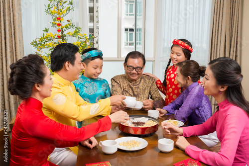Happy big Asian family in traditional costumes drinking tea and celebrating Lunar New Year