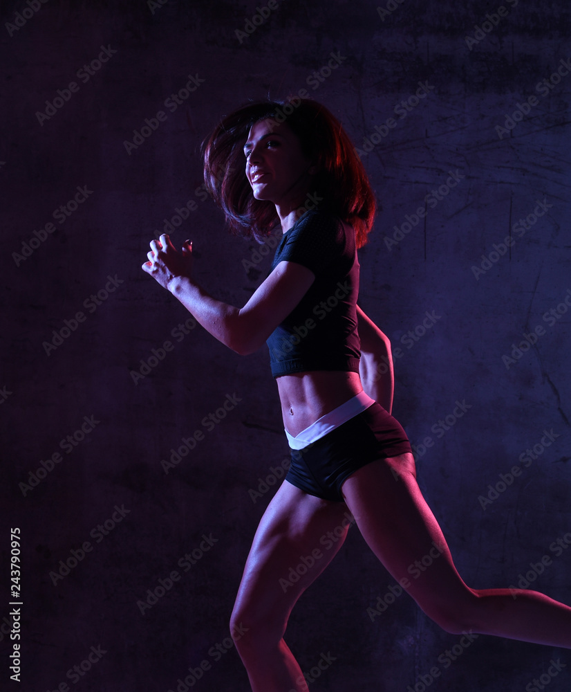 Young sport woman running jogging in gyn in blue and pink neon light on dark wall 