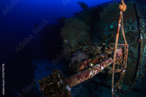 SCUBA divers exploring a deep, underwater shipwreck in a clear, tropical ocean