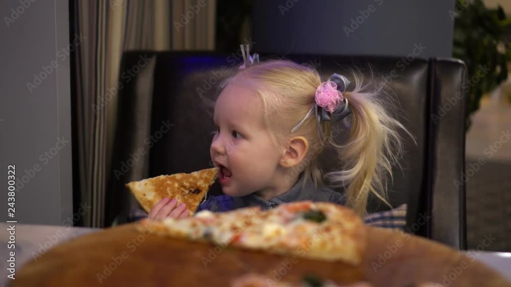 A little girl eating pizza in a cafe. A little girl eating pizza in a cafe.