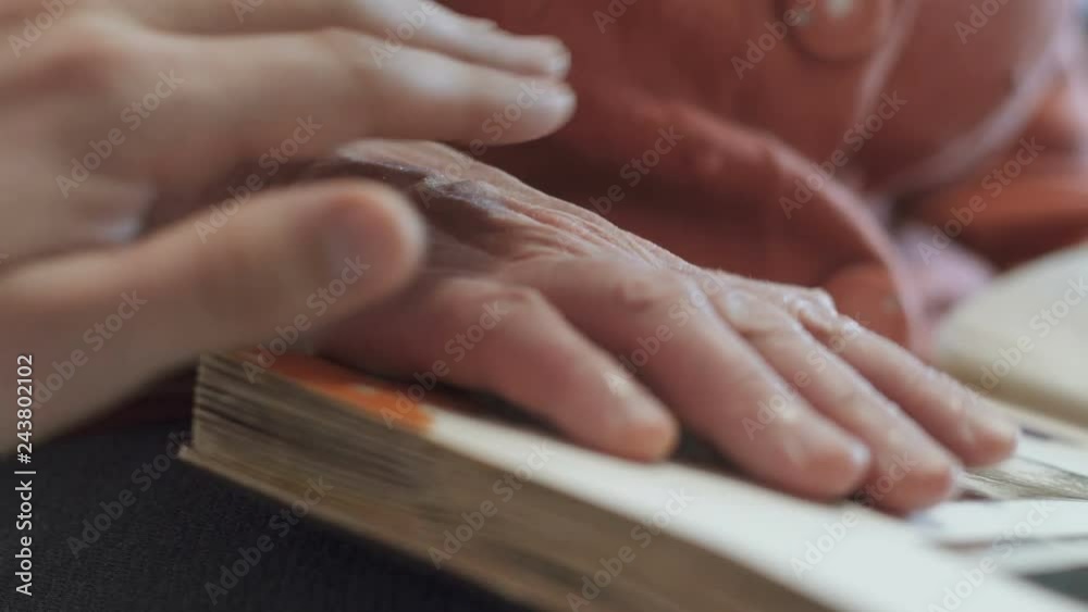 An elderly woman looks at photos in a photo album, and her grandson calms her grandmother An elderly woman looks at photos in a photo album, and her grandson calms her grandmother