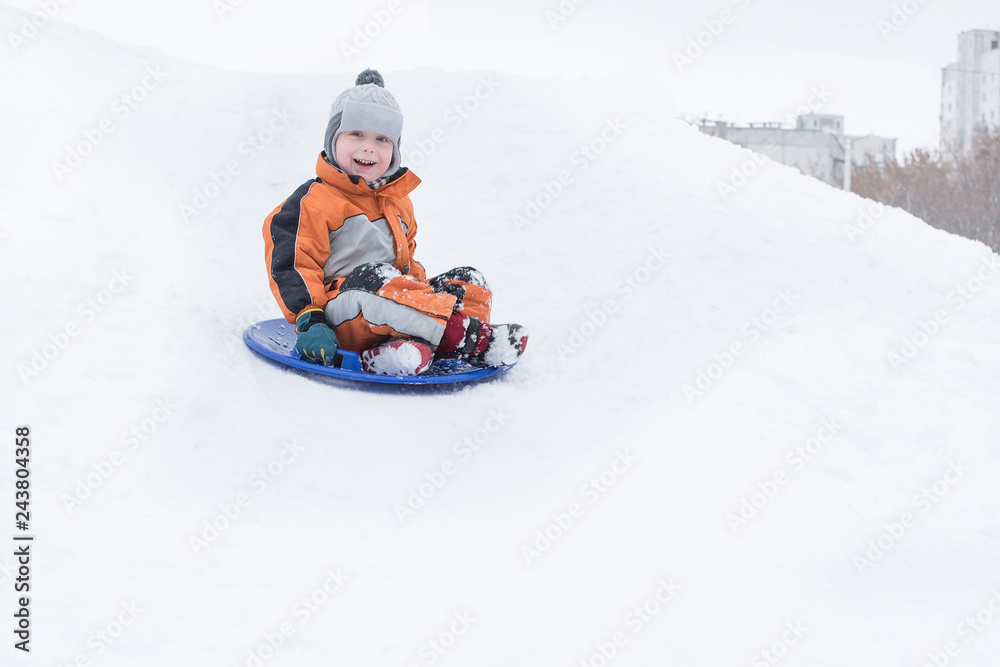 Happy laughing small boy slides down the hill on snow saucer. Seasonal concept. Winter day.
