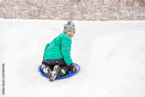 Happy laughing boy slides down the hill on snow saucer. Seasonal concept. Winter day