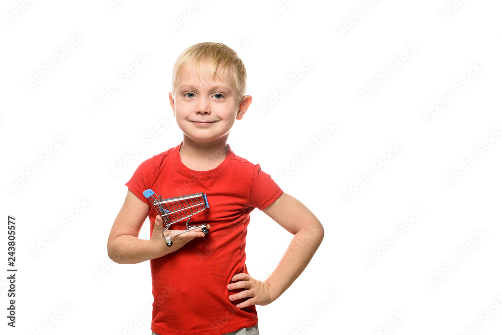 Shopping concept. Blond cute little smiling boy in red t-shirt holding a small metal shopping trolley. Isolate on white background.