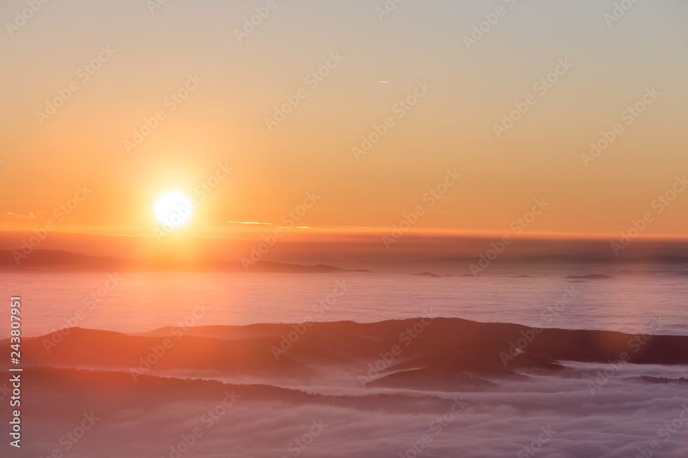 Obraz premium Beautiful sunset over a valley filled by fog with mountains and hills