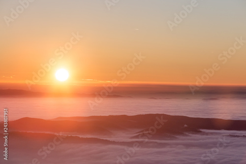 Beautiful sunset over a valley filled by fog with mountains and hills
