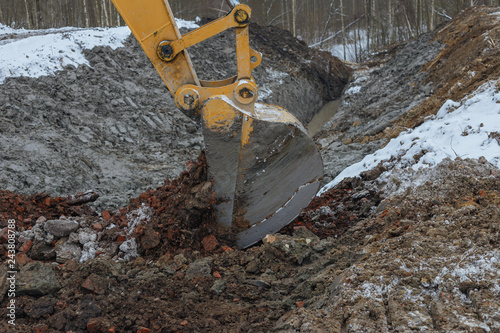 the process of loosening the soil with an excavator bucket during land reclamation work in the spring forest