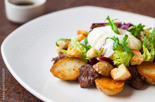Warm salad with chicken, grilled potatoes, crackers, arugula, grated cheese and poached egg on a white plate and soy dressing. Close up. Selective focus. The concept of the menu.
