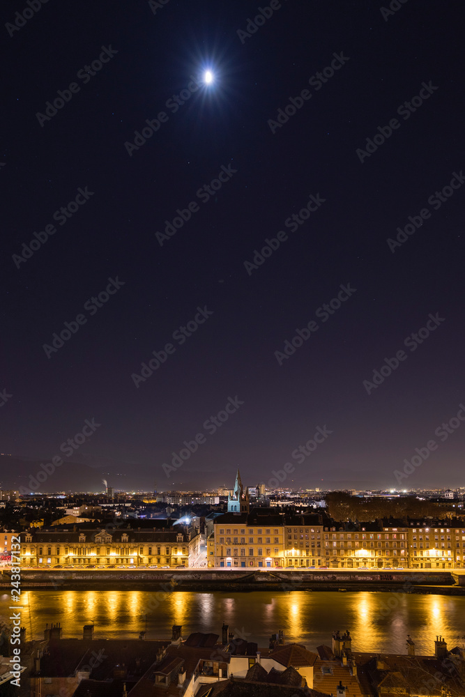 Grenoble, France, January 2019 : City at night with isere river, the moon and stars in the sky
