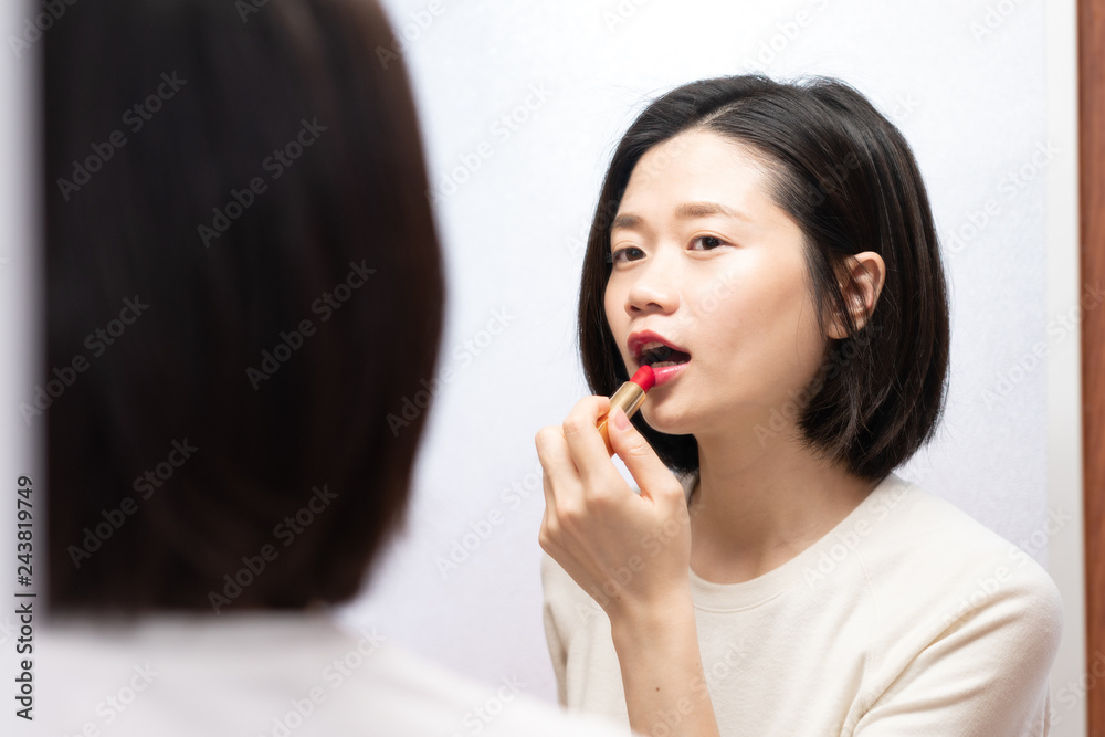 asian female applying makeup and looking in mirror asian female applying makeup and looking in mirror