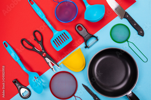 Close up portrait of frying pan with set of kitchen utensils on red-blue background