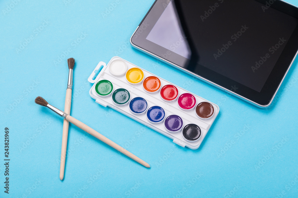 Watercolor paints and brush with tablet on blue background Watercolor paints and brush with tablet on blue background