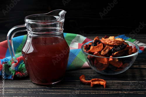 Compote of dried fruit in a jug, transparent plate with dry fruit on a dark wooden background.