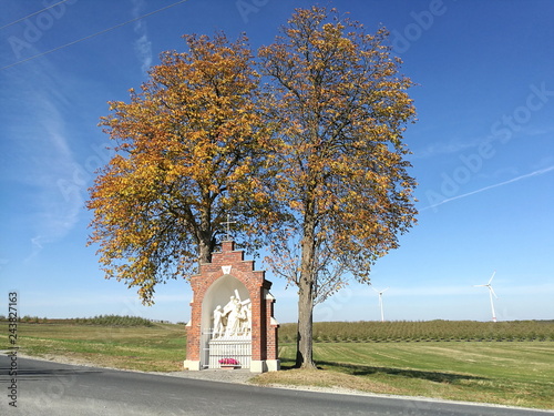 Herbstliche alte Bäume mit religiösem Denkmal vor blauem Himmel im Sonnenschein an einem alten Pilgerweg in Stromberg bei Oelde im Kreis Warendorf im Münsterland in Westfalen photo