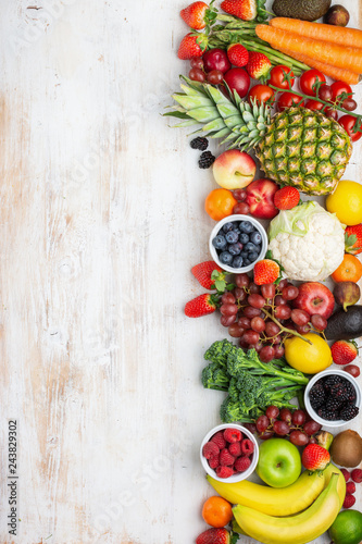 Fototapeta Naklejka Na Ścianę i Meble -  Healthy colorful fruits vegetables berries, strawberries oranges plums grapes broccoli cauiliflower mango persimmon pineapple on white wooden table, top view, copy space, vertical, selective focus