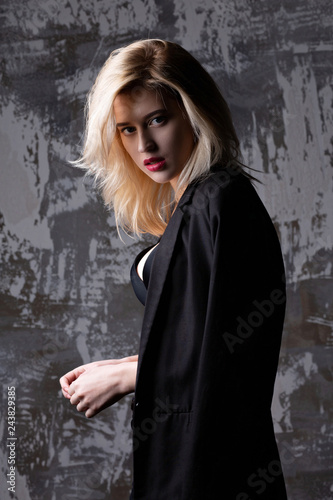 Magnificent blonde model wearing jacket and bra posing at studio with shadows
