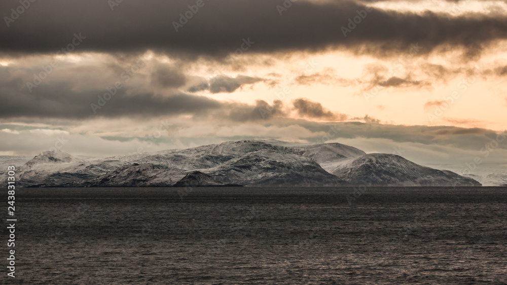 A snowy mountain on the water. The sun leaves behind golden clouds. A snowy mountain on the water. The sun leaves behind golden clouds.