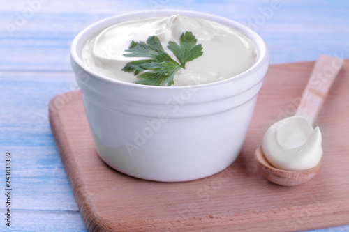 Mayonnaise in a white bowl and in a spoon on a board on a blue wooden background. white sauce. close-up