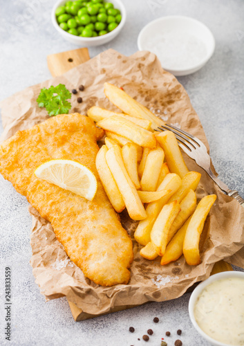Photography Traditional British Fish and Chips with tartar sauce on chopping board with fork and green peas on white stone table background