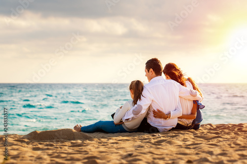 Young family sitting together in late afternoon sun on beach.