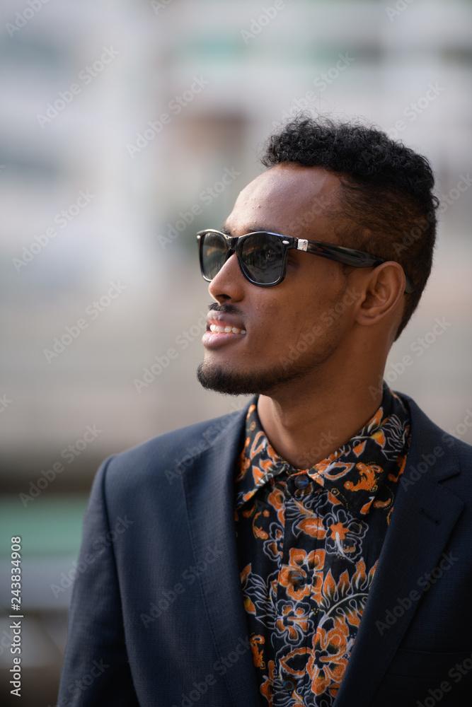 Face of happy young African businessman with sunglasses thinking outdoors Face of happy young African businessman with sunglasses thinking outdoors