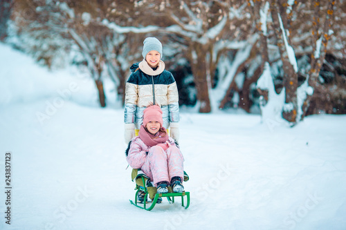 Adorable little happy girls sledding in winter snowy day.