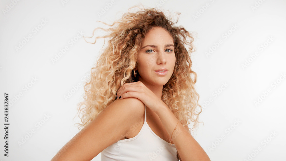 head and shoulders plan of model with big curly blonde hair in studio and blowing hair with serious face watching to the camera head and shoulders plan of model with big curly blonde hair in studio and blowing hair with serious face watching to the camera