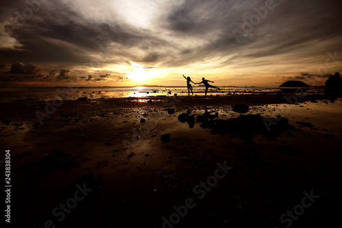 A pair of young people are having fun running on the beach at sunset.