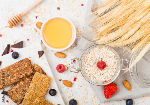 Organic cereal granola bar with berries on marble board with honey spoon and jar of oats and linen towel on marble background. Raw wheat bundle photo